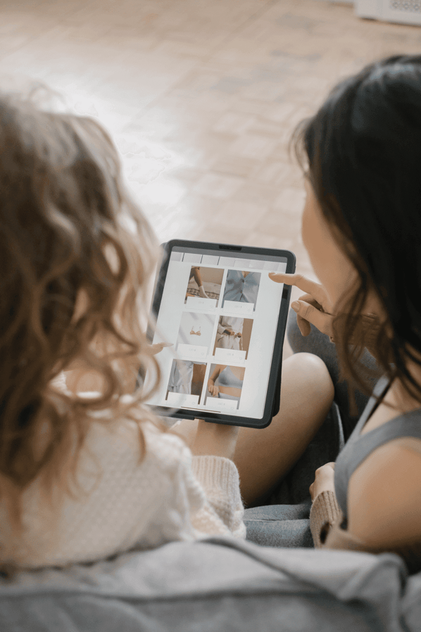 Two women sitting on a couch looking at a tablet displaying a webpage selling nightwear