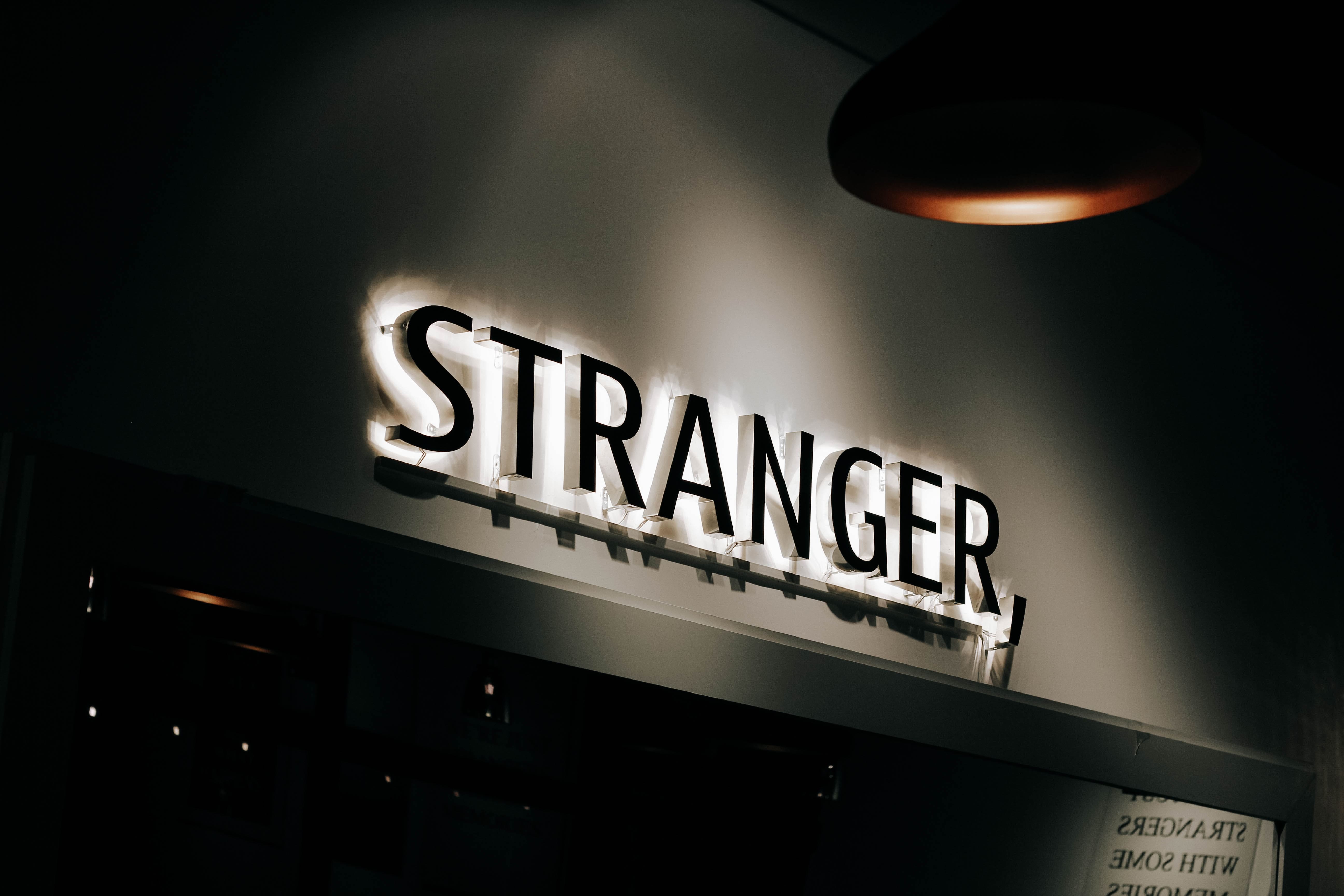 Lit up sign in a dark room reading "STRANGER"